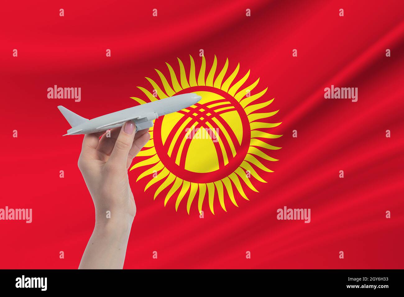 Airplane in hand with national flag of Kyrgyzstan Travel to Kyrgyzstan. Stock Photo