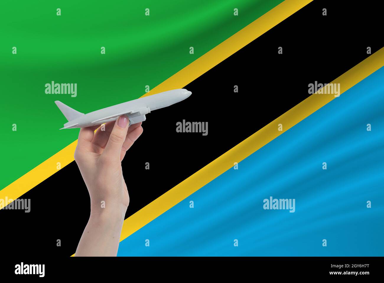 Airplane in hand with national flag of Tanzania. Travel to Tanzania. Stock Photo