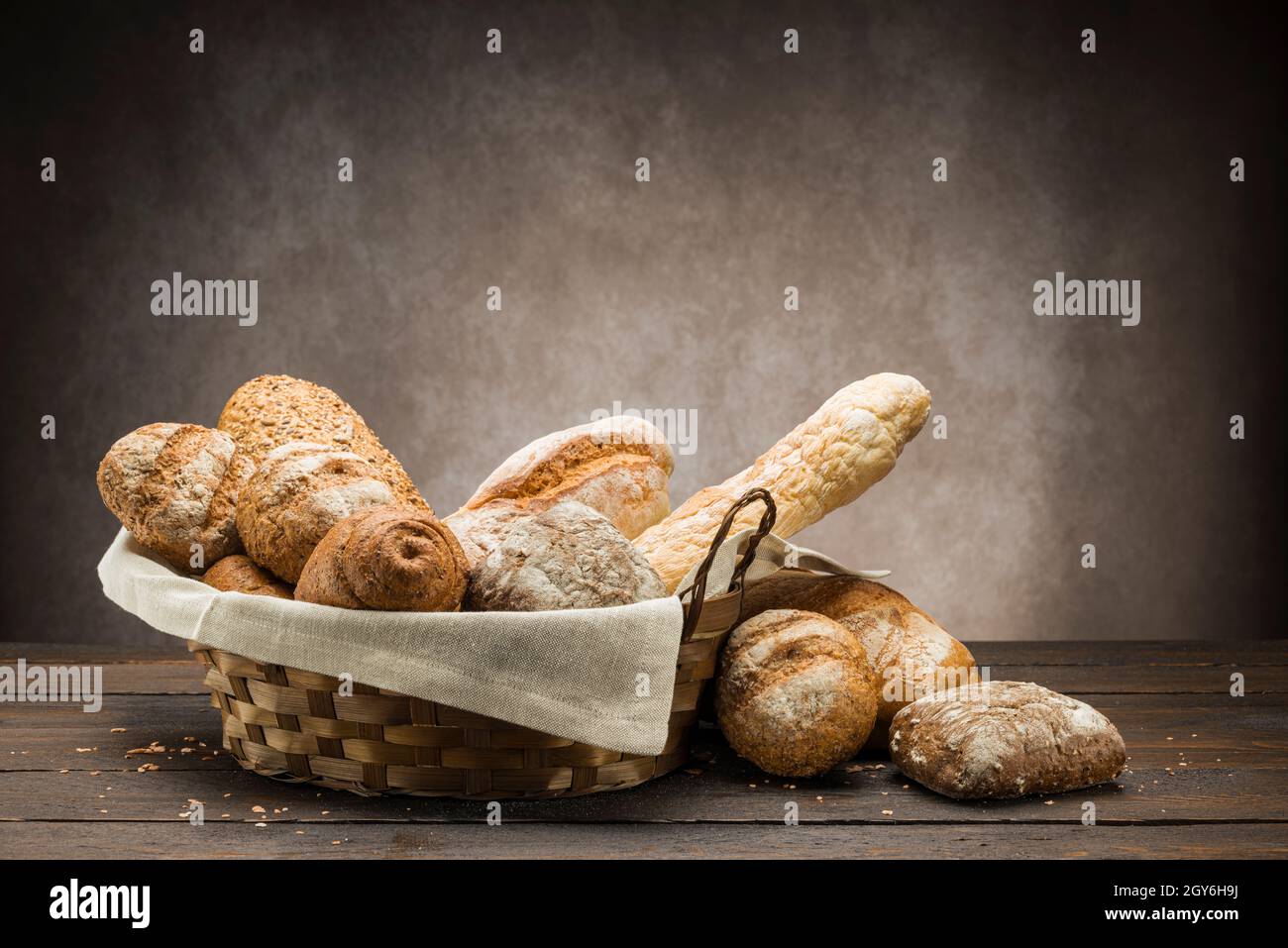 assortment of baked bread in straw basket on wooden table Stock Photo