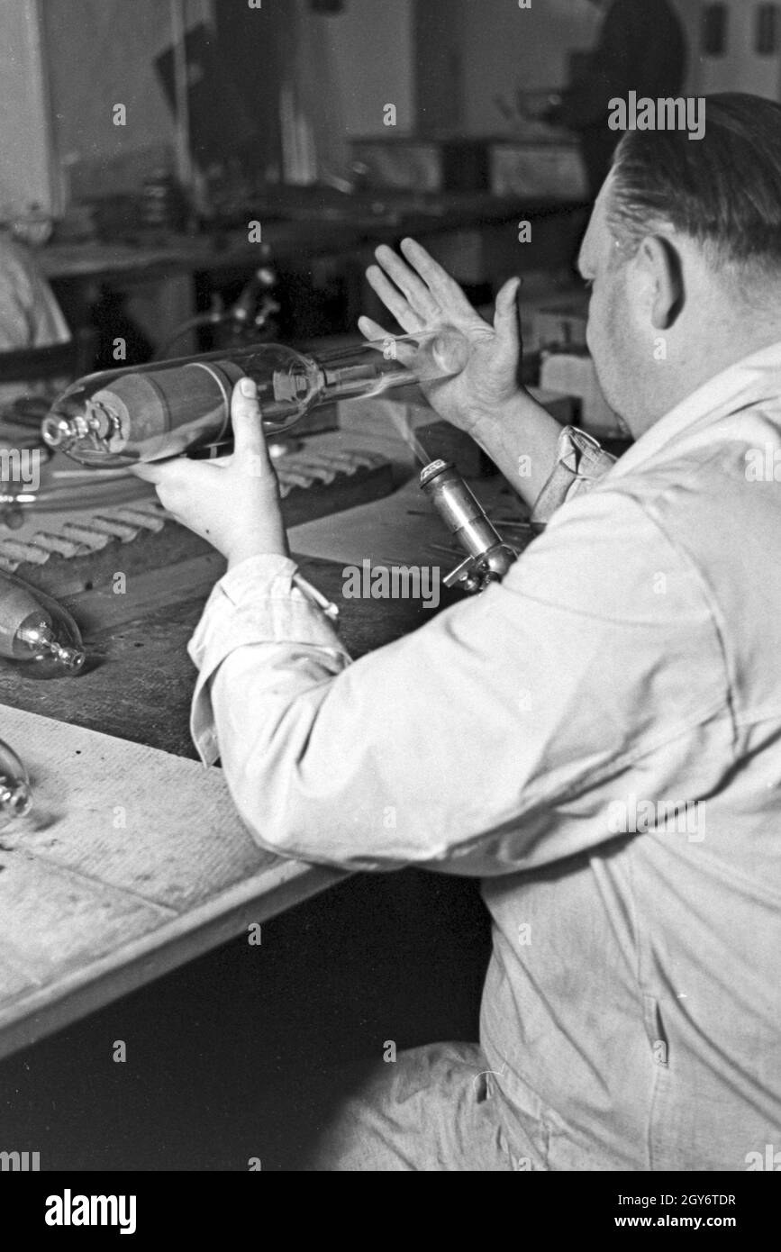 Ein Mitarbeiter einer Leuchtröhrenfabrik bei der Herstellung einer Leuchtöhre, Deutschland 1930er Jahre. A staff member producing a fluorescent tube, Germany 1930s. Stock Photo