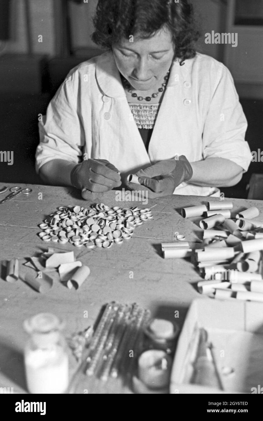 Eine Mitarbeiterin einer Leuchtröhrenfabrik sortiert elektrische Kontakte, Deutschland 1930er Jahre. A female staff member of a factory of fluorescent tubes assorting electrical buttons, Germany 1930s. Stock Photo