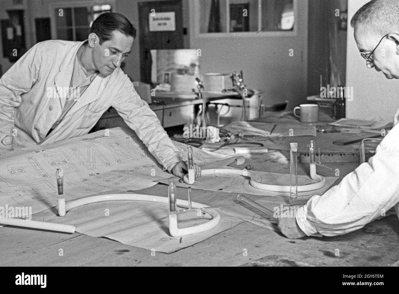 Zwei Mitarbeiter einer Leuchtröhrenfabrik bei der Herstellung einer Leuchtöhre, Deutschland 1930er Jahre. Two staff members producing a fluorescent tube, Germany 1930s. Stock Photo
