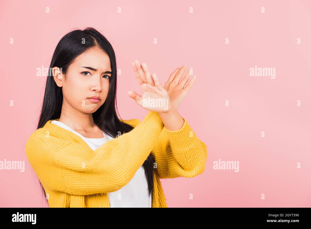 Portrait Asian beautiful young woman unhappy or confident standing wear holding two cross arms say no X sign, studio shot isolated pink background, Th Stock Photo