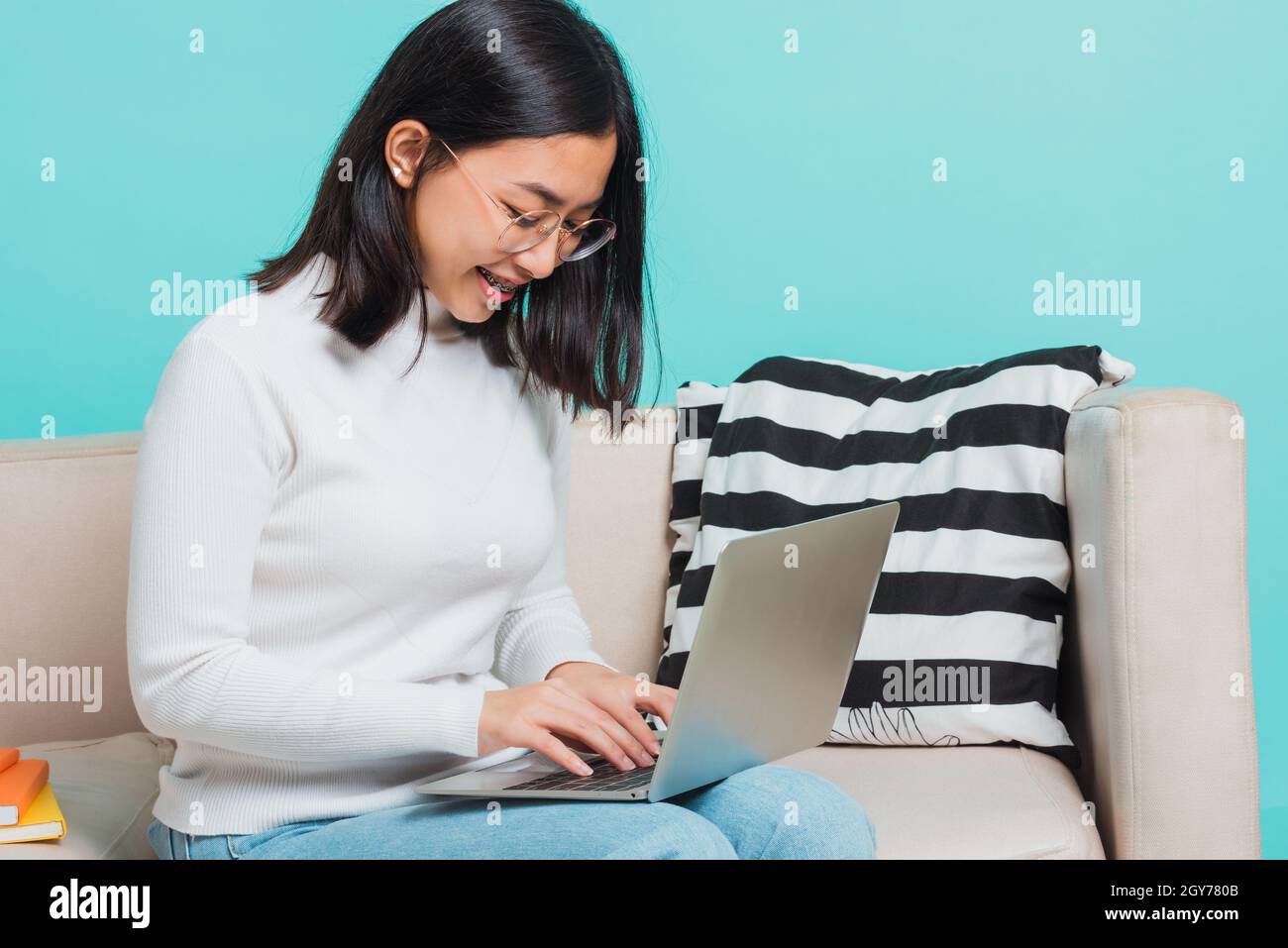 Asian beautiful young woman wear eyeglasses sitting on sofa using a laptop, portrait relaxation of happy female smiling in living freelancer working o Stock Photo