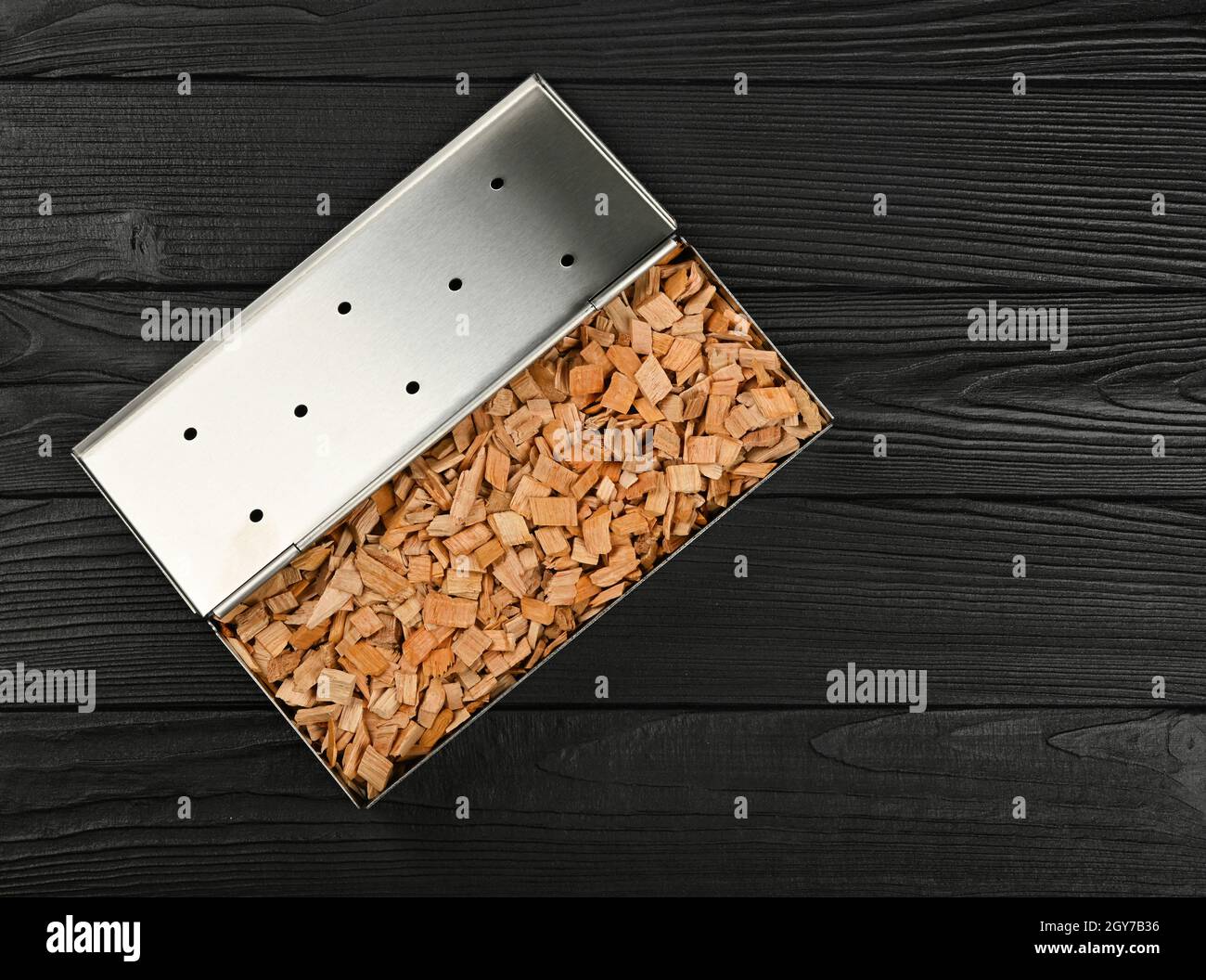Close up one stainless steel metal smoker box with hardwood alder chips on black wooden table, ready to barbecue grill and smoke food, elevated top vi Stock Photo