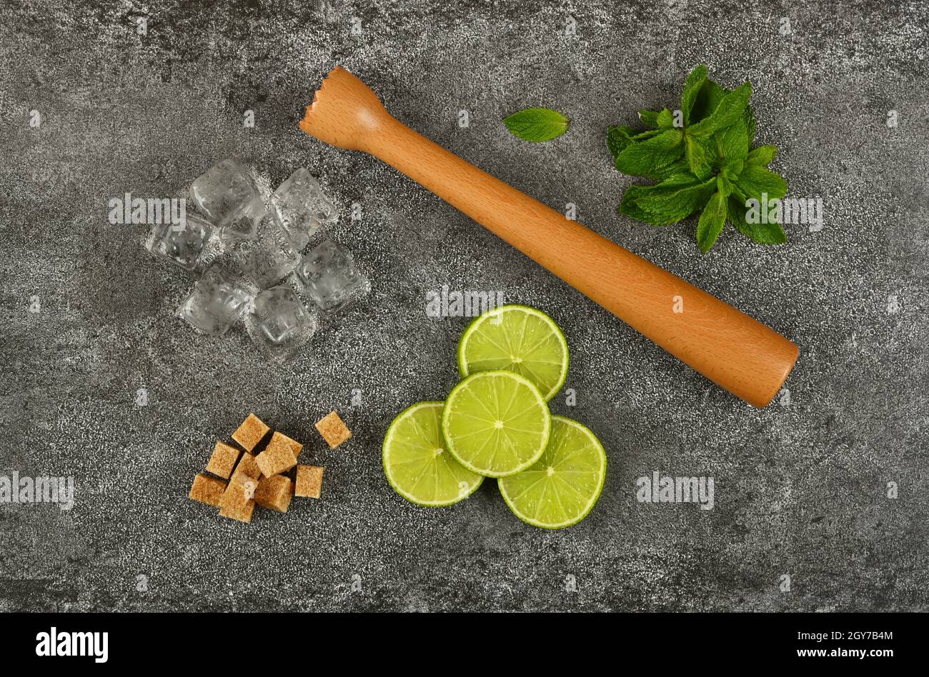 Close up mojito cocktail ingredients set flat lay, wooden muddler, brown sugar, heap of fresh green mint leaves, lime slices and ice cubes on table, e Stock Photo