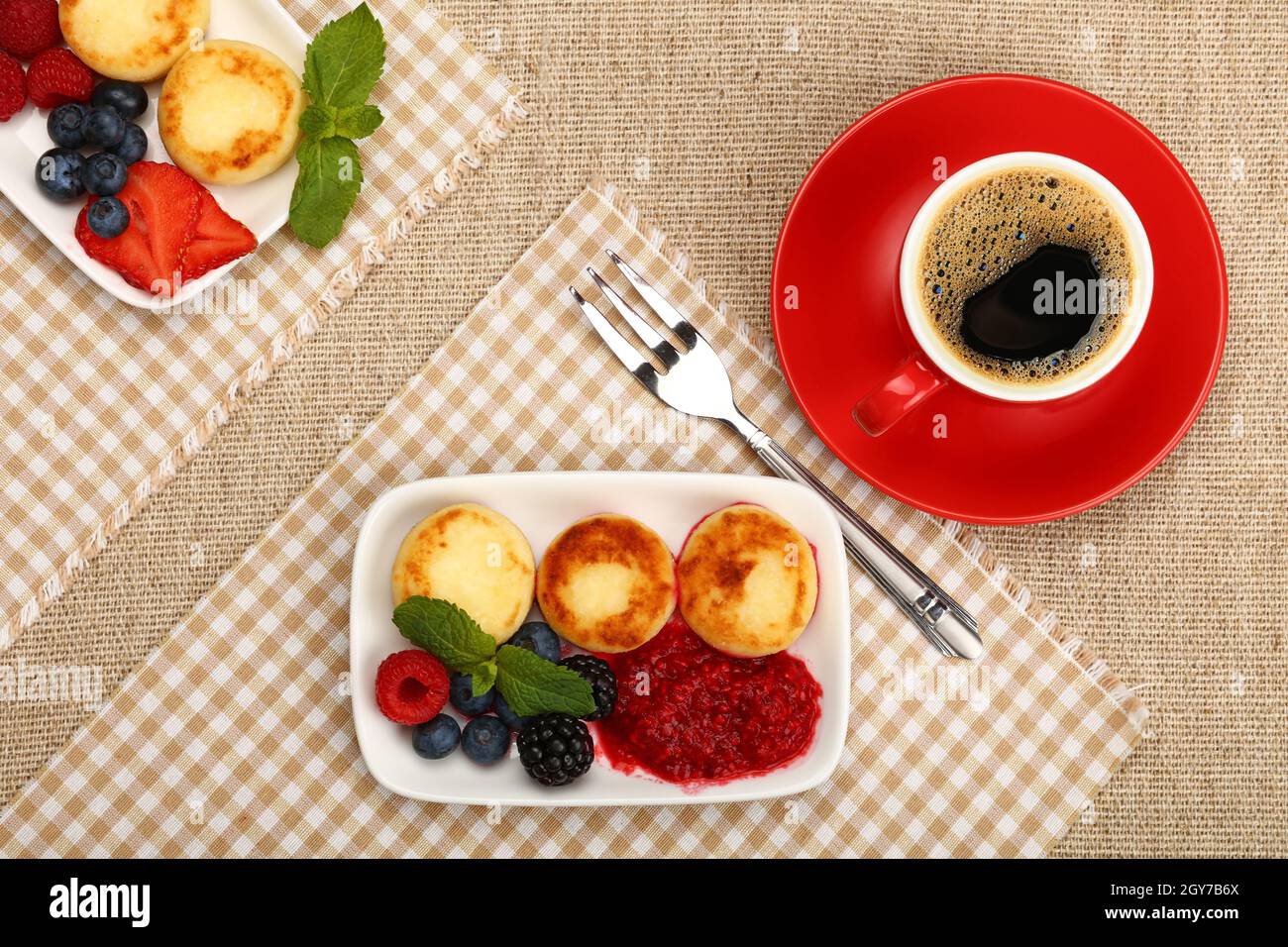 Close up serving portion of European quark cheese pancakes dessert with fruits and cup of black coffee, elevated top view, directly above Stock Photo