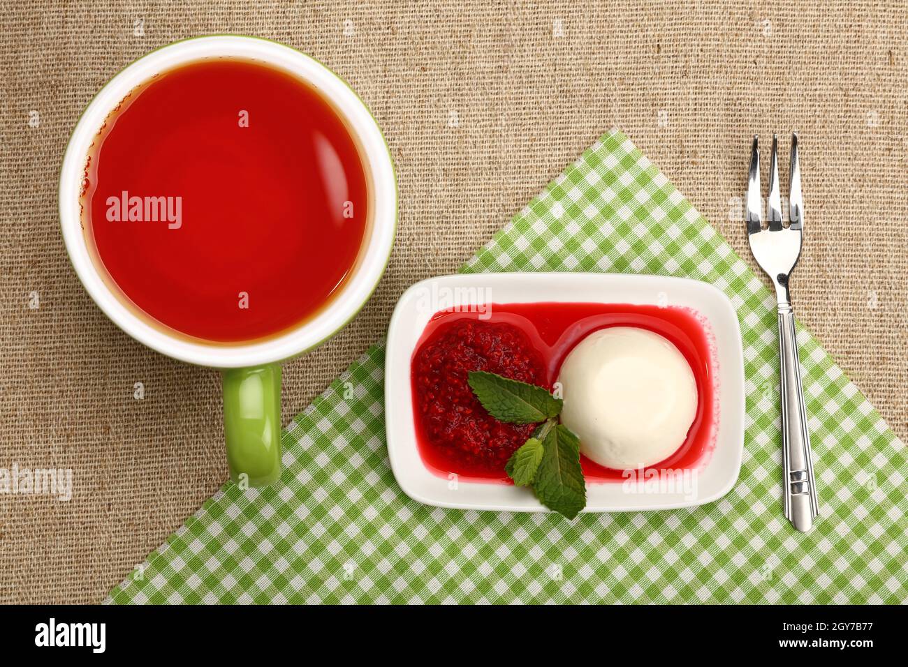 Close up serving panna cotta traditional Italian dessert with raspberry jam and cup of red black tea, elevated top view, directly above Stock Photo