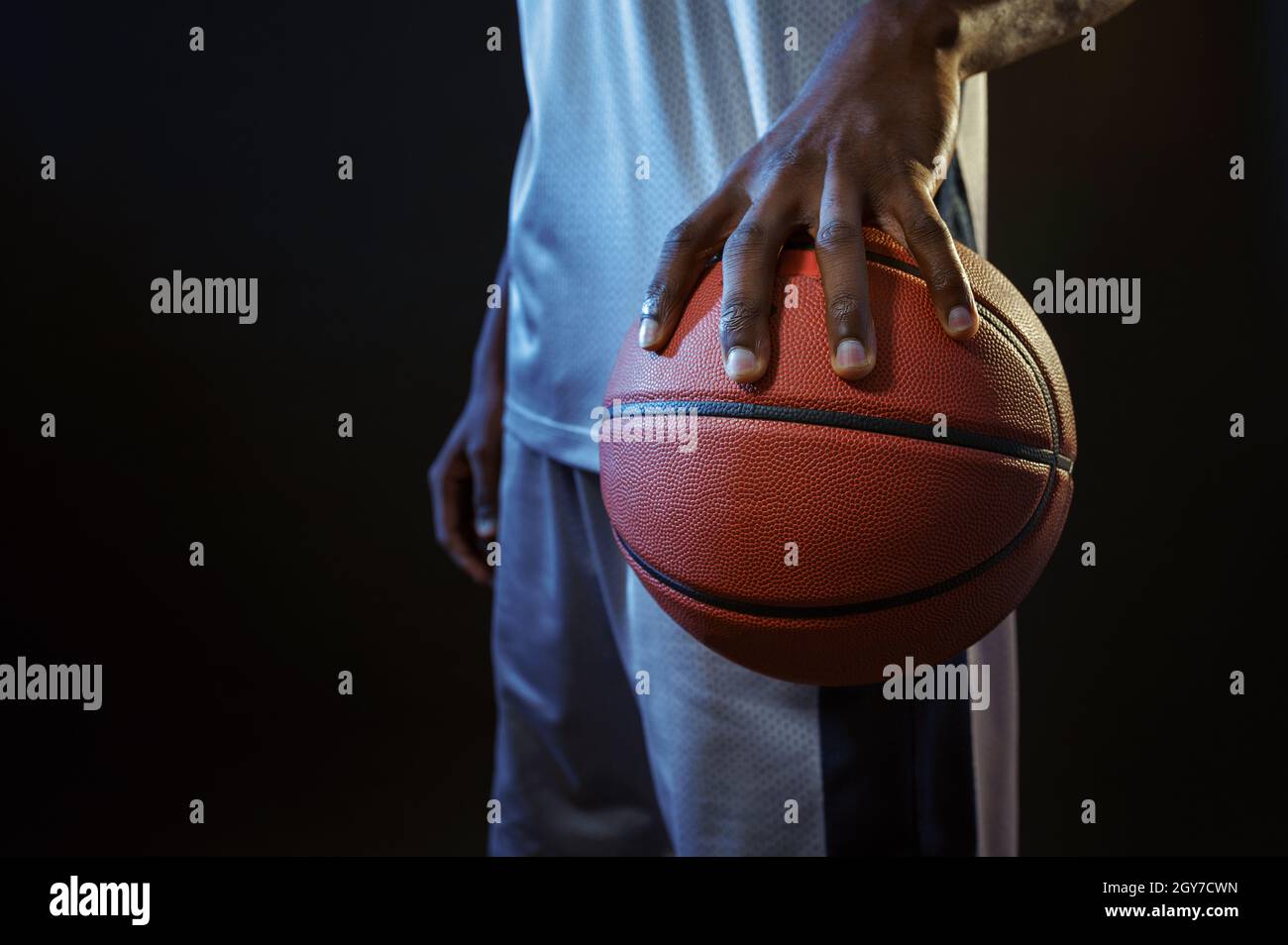 Strong basketball player hand holds ball in studio, black background