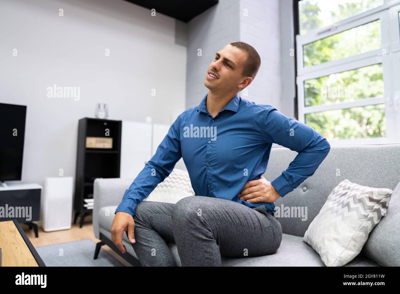 Man Sitting On Sofa Having Back Pain Stock Photo