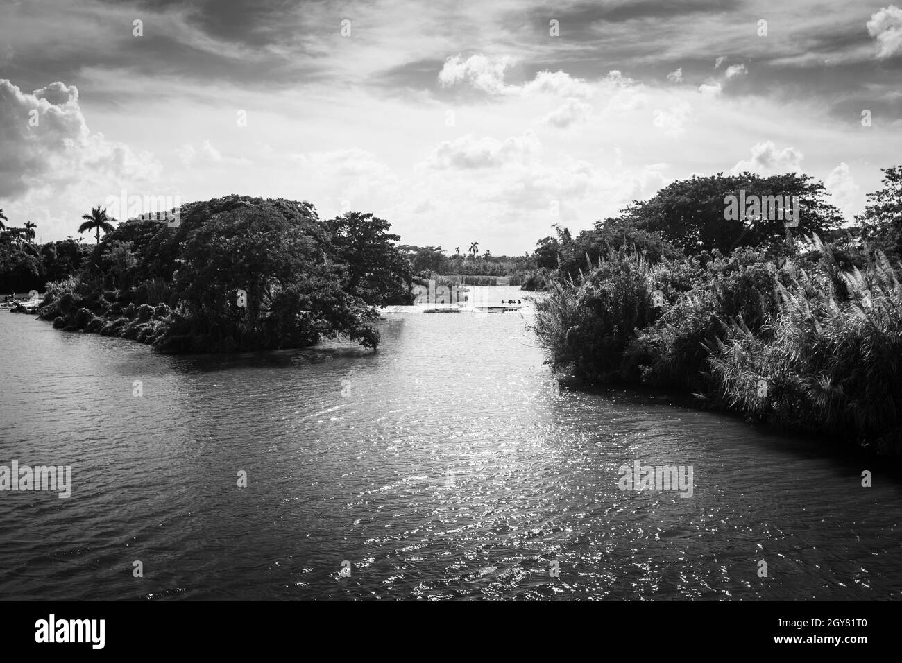 A view black and white of a river that folks, with the strong sunlight and a far group of people taking a bath surrounded by the virgin nature. Stock Photo