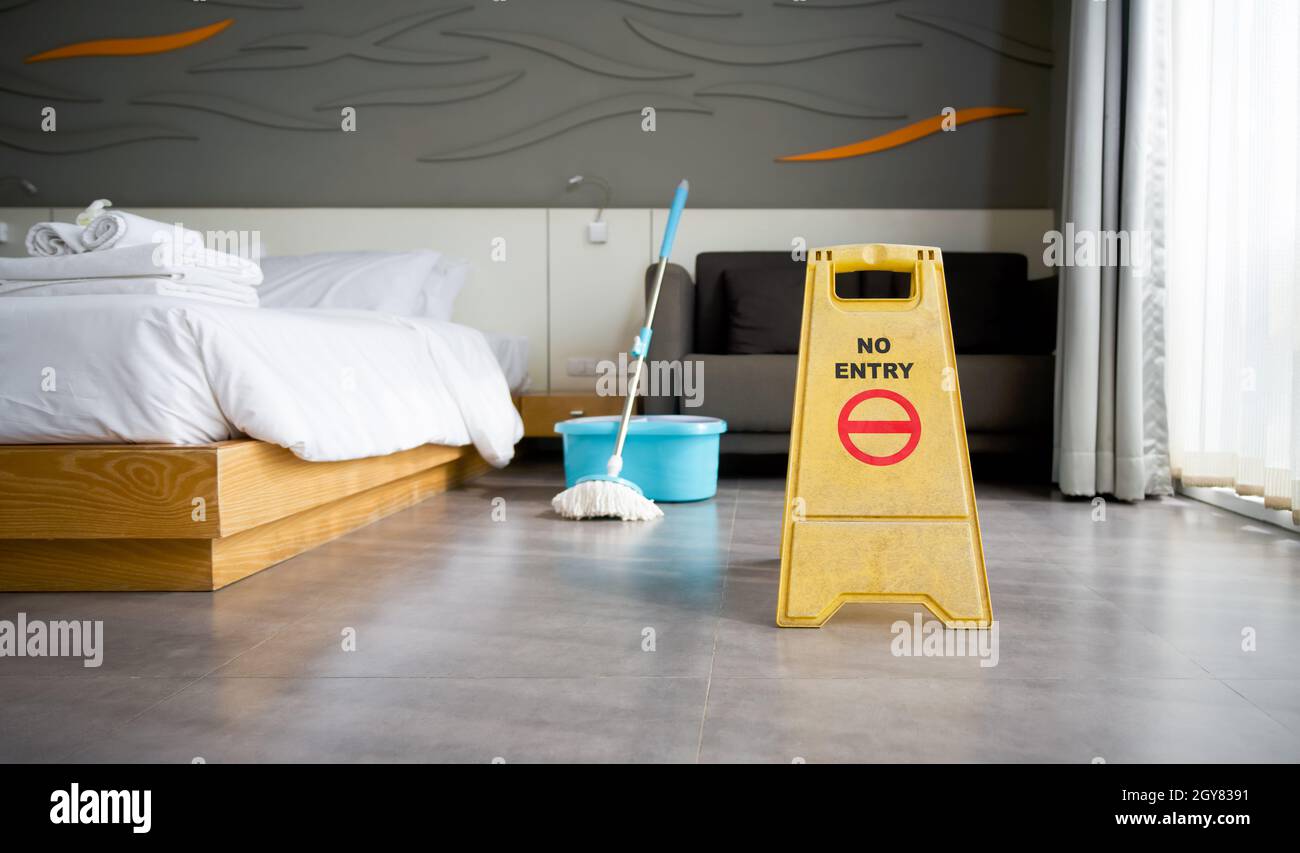 A yellow "NO ENTRY" sign place on the floor in hotel room. While cleaning.  A mop and a bucket of water in the background Stock Photo - Alamy