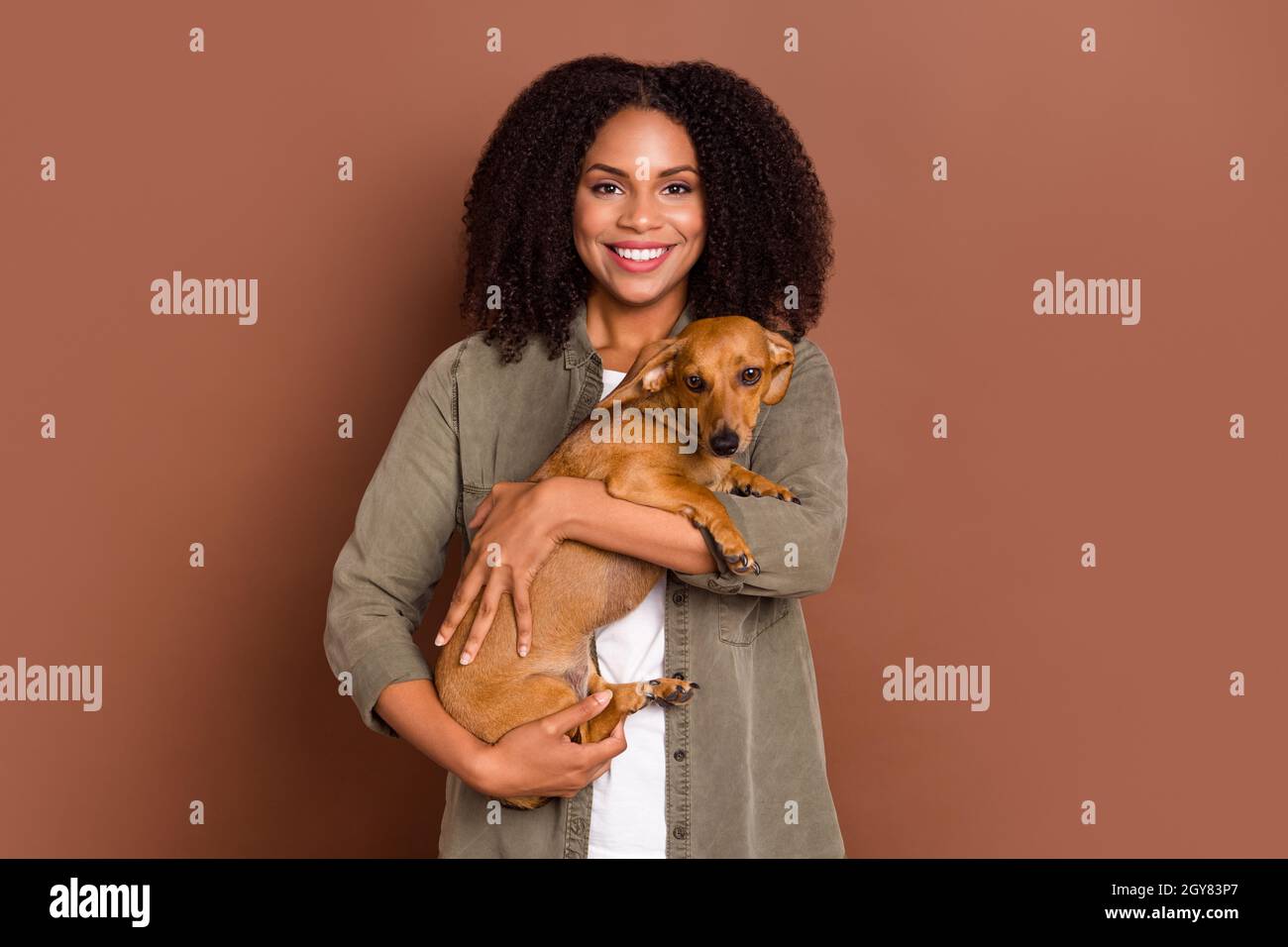 Photo of funny young brunette lady hold dog wear shirt isolated on brown color background Stock Photo