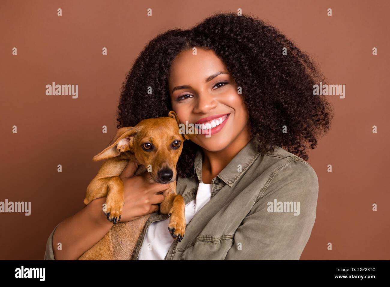 Portrait of adorable girl holding hands pup toothy smile look camera have good mood isolated on brown color background Stock Photo