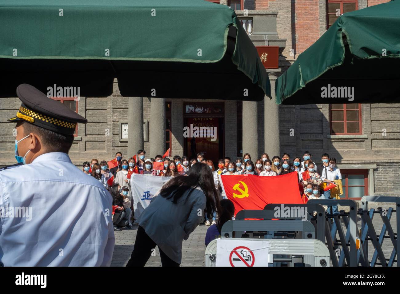 Chinese Communist Party members from a university have a group photo with a party flag in front of the historical Red Building of Peking University in Stock Photo