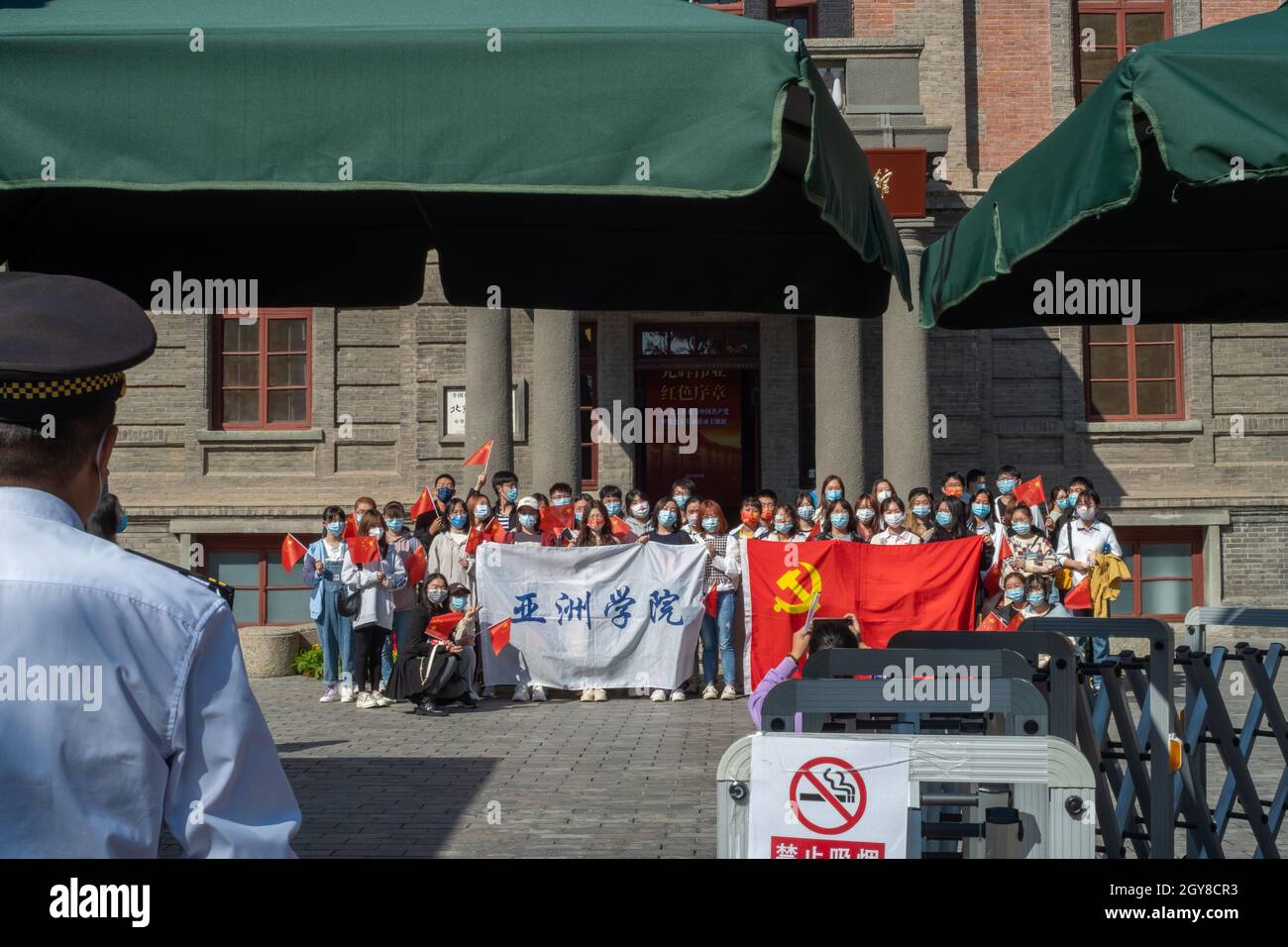 Chinese Communist Party members from a university have a group photo with a party flag in front of the historical Red Building of Peking University in Stock Photo