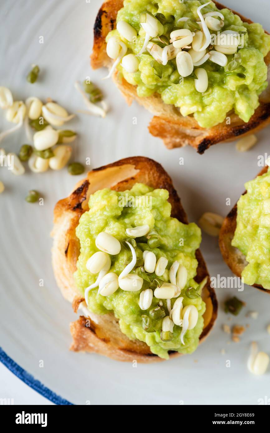 Avocado and bean sprouts appetizer toasts on plate, top view Stock Photo