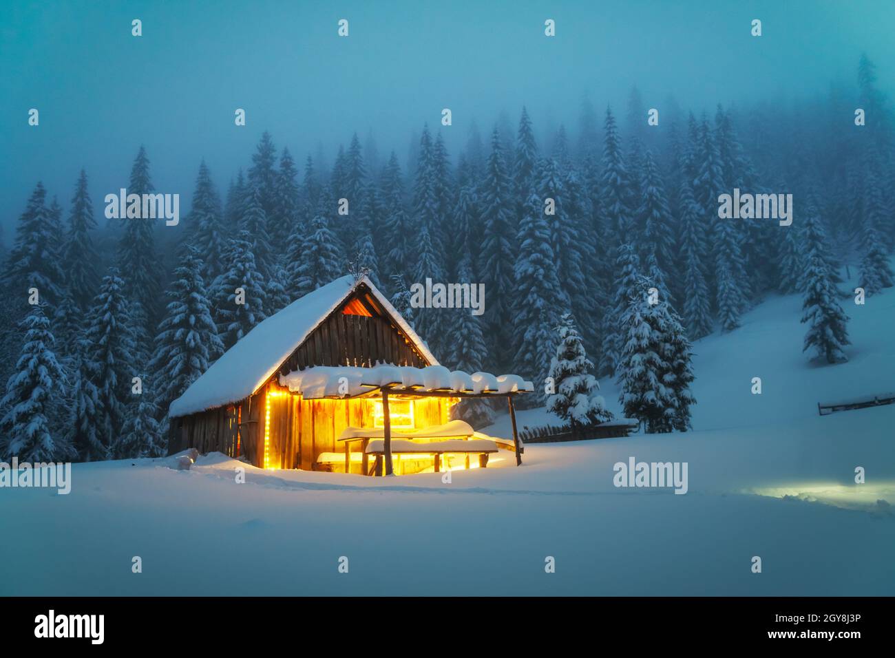 Fantastic winter landscape with glowing wooden cabin in snowy forest ...