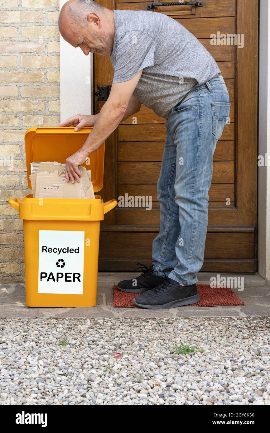 a man puts cardboard in the paper recycling bin in front of his house Stock Photo