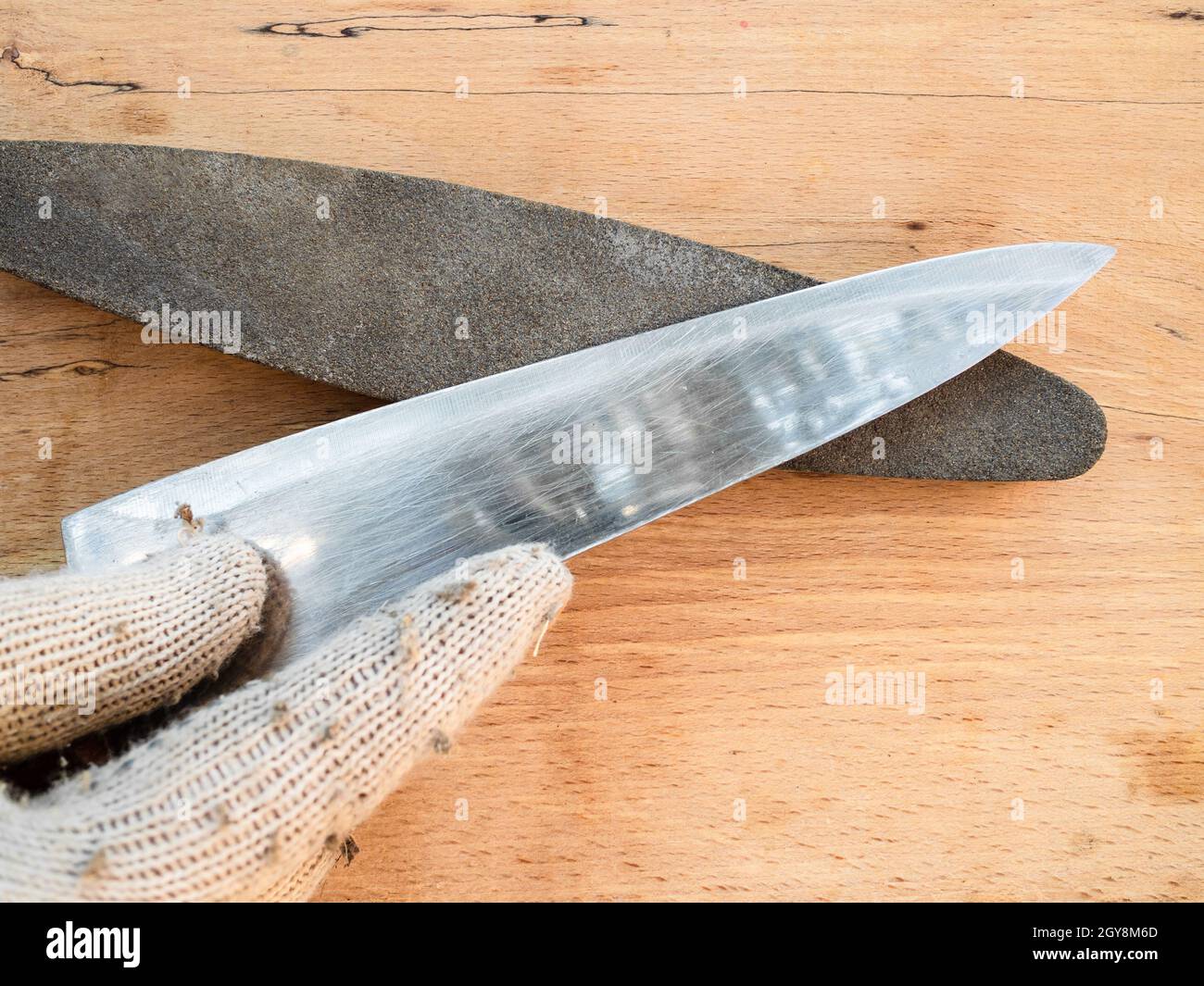 gloved hand sharpens kitchen knife closeup on whetstone Stock Photo