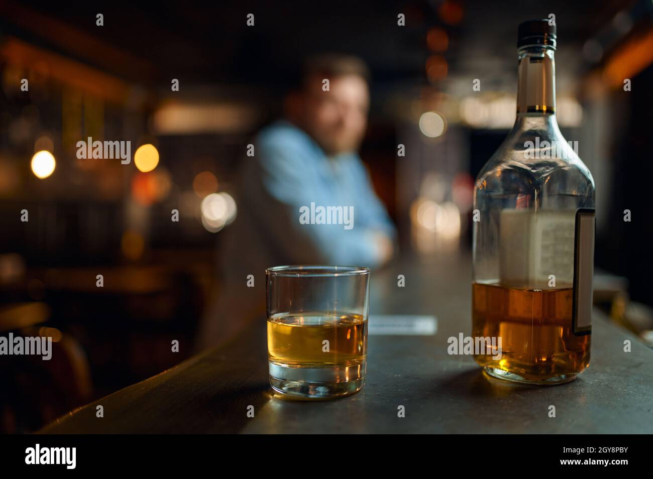 Bottle of alcohol and glass on counter in bar, male person on dlur background. Man resting in pub, human emotions and leisure activities, stress relie Stock Photo
