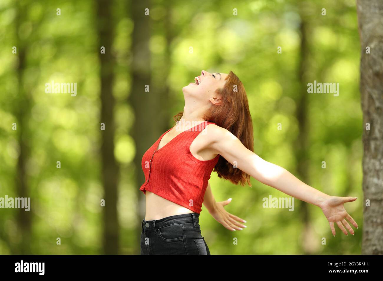 Profile of an excited woman stretching arms screaming loud in a forest ...