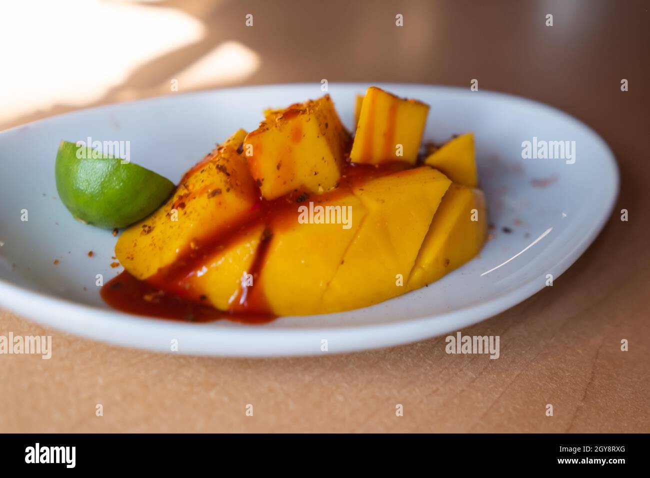 Plate of chopped mango with Mexican chamoy sauce and blurry background