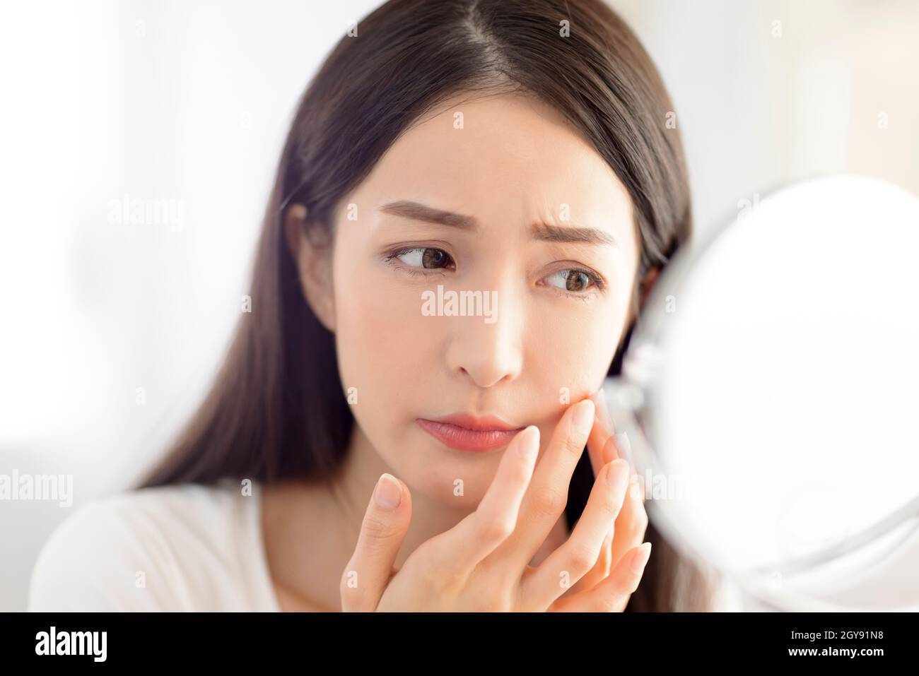 Young woman looking at mirror and checking the acne problem at home