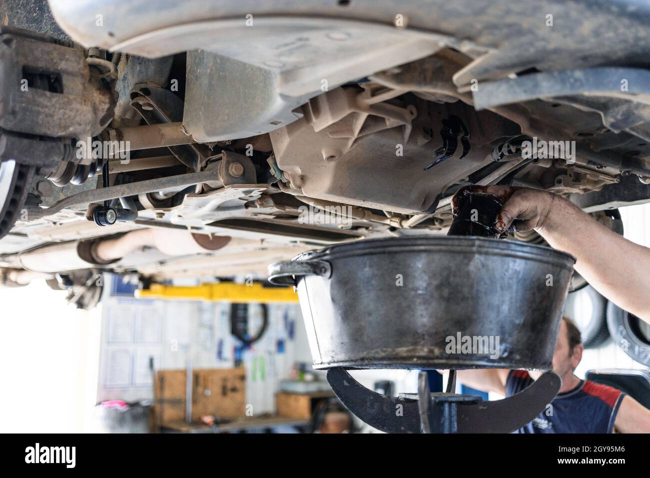 mechanic drains old engine oil from lifted car in car Stock