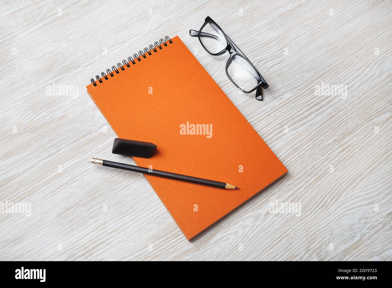 Orange notebook, glasses, pencil and eraser on light wood table background. Branding mock up. Stock Photo