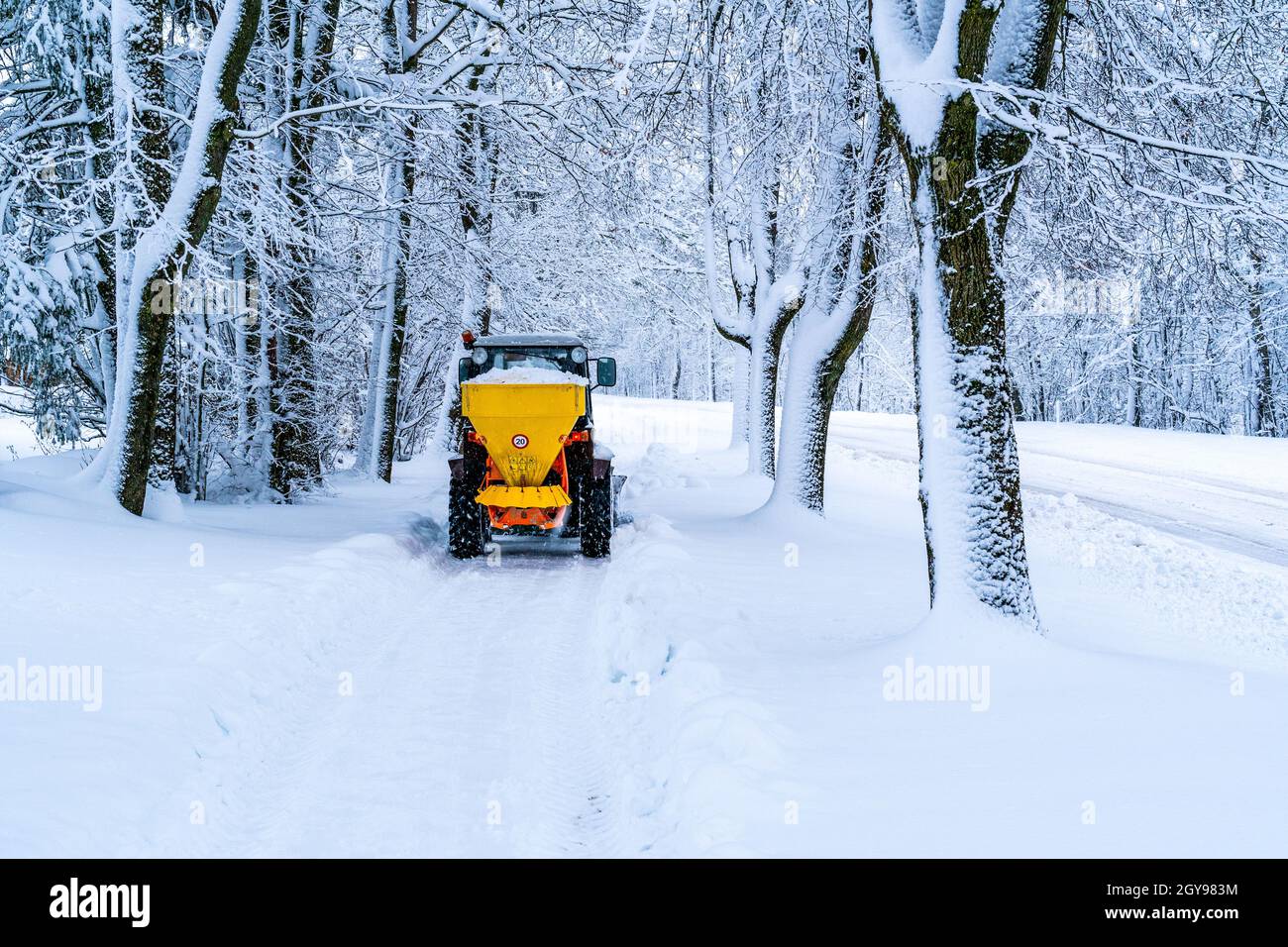 Tractor with mounted salt spreader, road maintenance - winter gritter vehicle. Tractor de-icing street, spreading salt. Municipal service melting ice Stock Photo