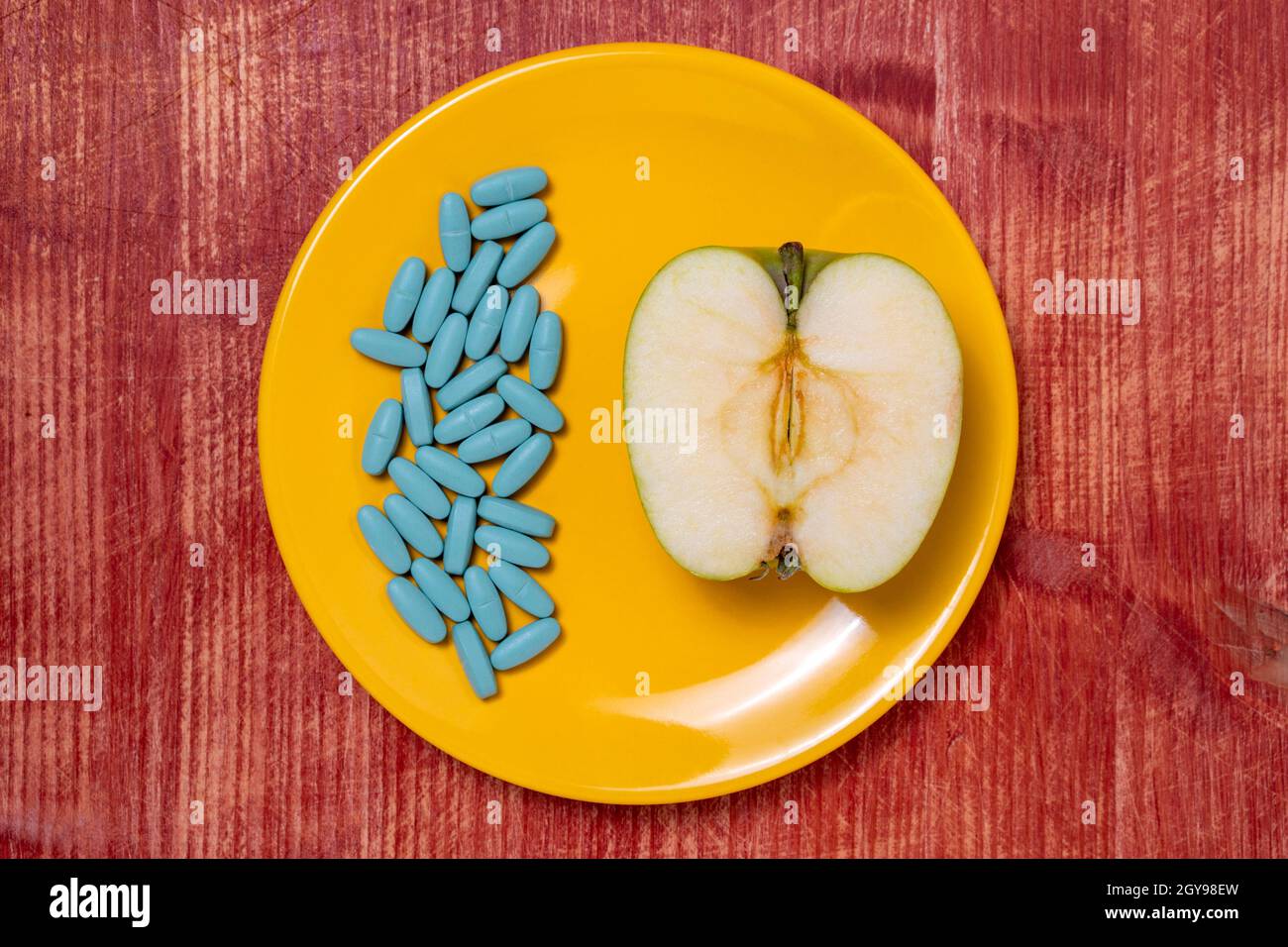 Drawing up a diet. Pills in a plate with an apple half on a wooden table.  Healthy eating, diet, lifestyle concept. Stock Photo