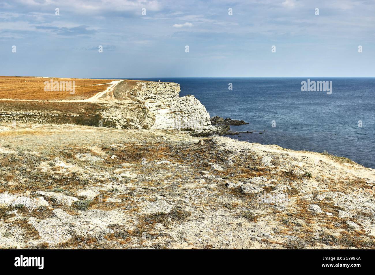 A country road along the edge of the cliff. Orange land, a cape by the sea. Seascape, horizon, calm blue sea, sky with advancing clouds. Chalk rocks. Stock Photo