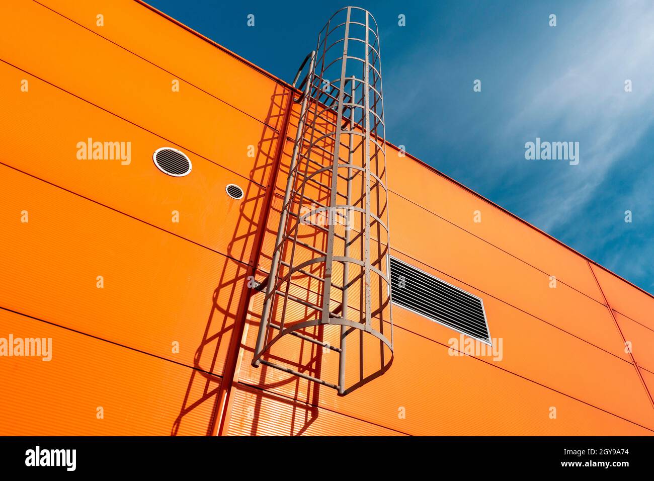 Orange industrial building wall with metal ladder,under blue sky Stock