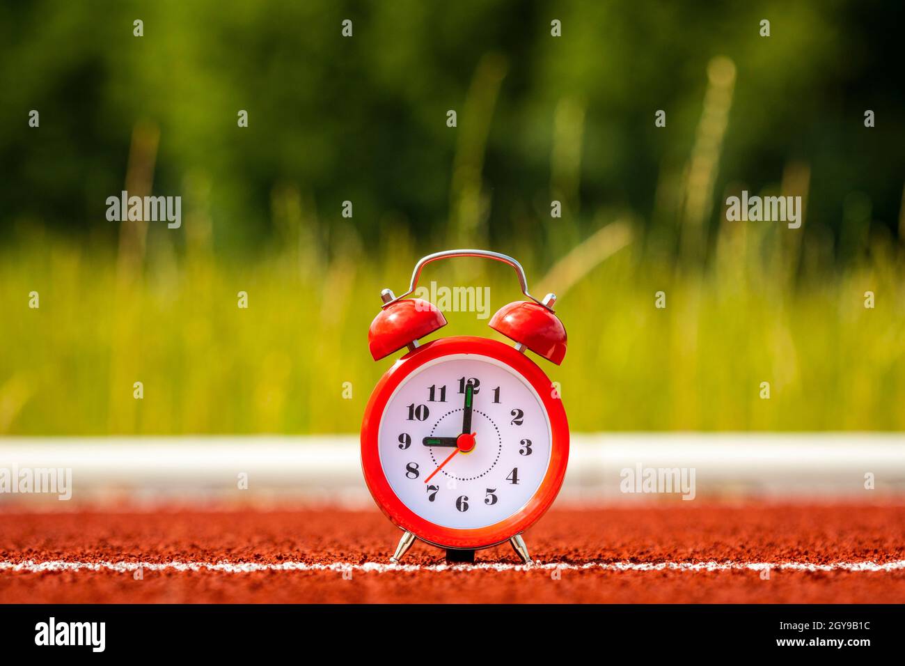 Red alarm clock on to the running track in the stadium. Stock Photo