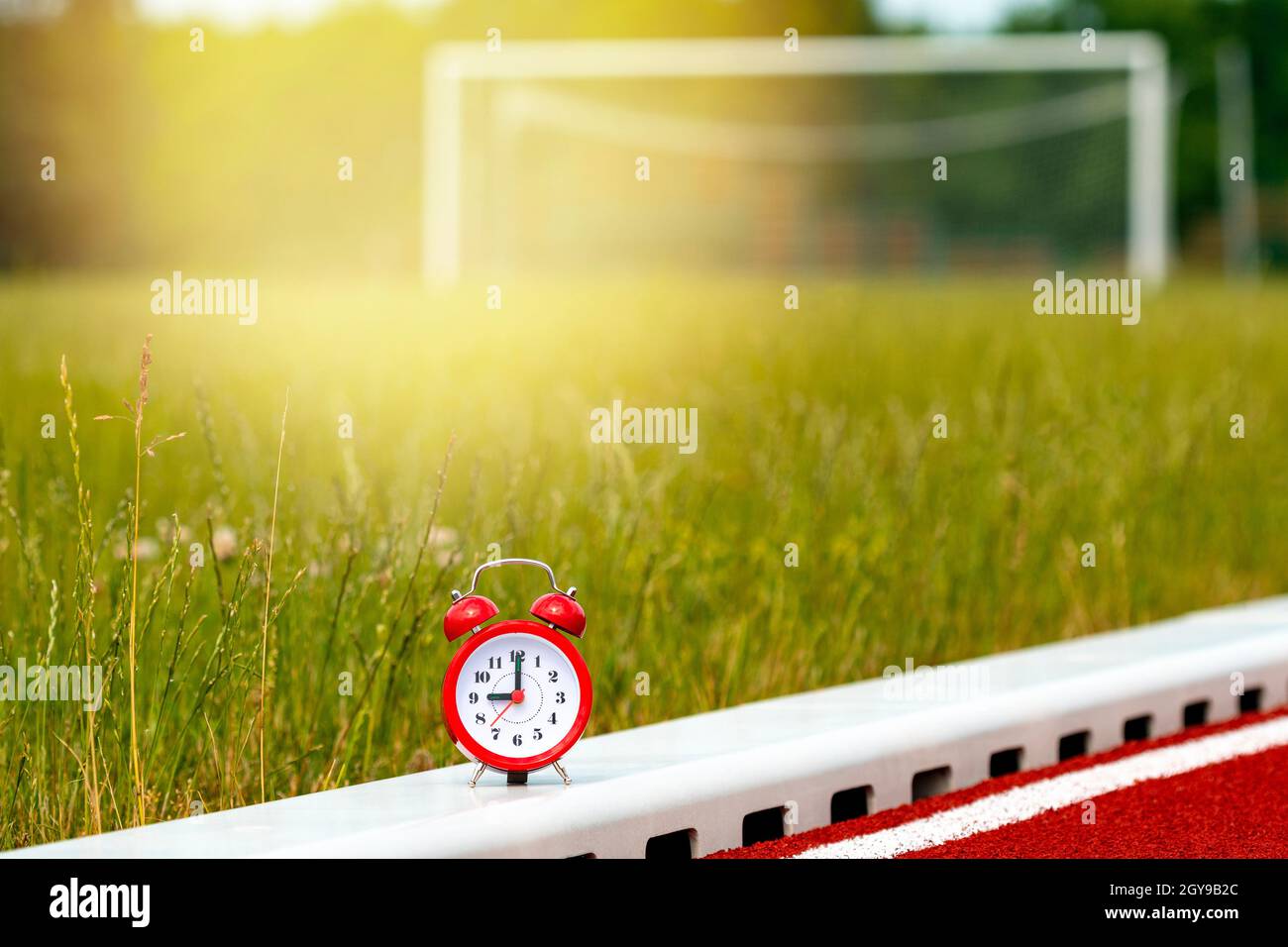 Red alarm clock on the football field with empty gate on background Stock Photo
