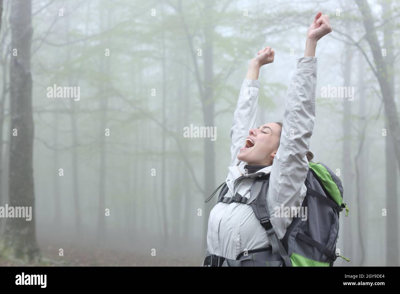 Excited trekker celebrating achievement in a foggy forest on vacation ...