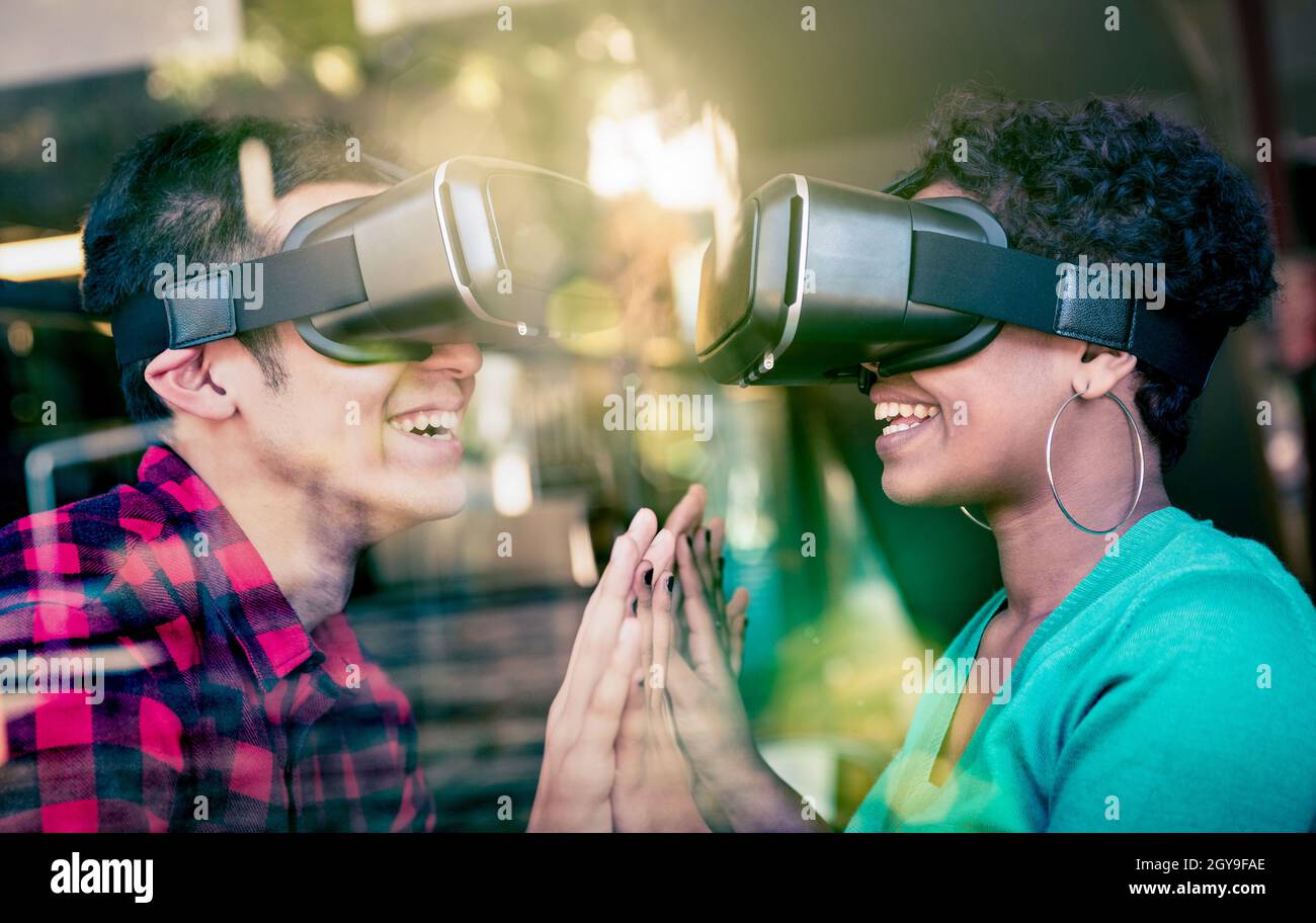 Multiracial couple in love going beyond racial diversity through virtual reality glasses - Young people having fun using new technology Stock Photo