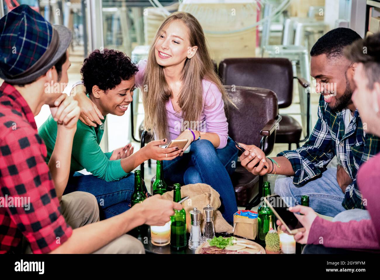Multiracial friends group drinking beer and having fun with phones at cocktail bar restaurant - Friendship concept with people enjoying time together Stock Photo