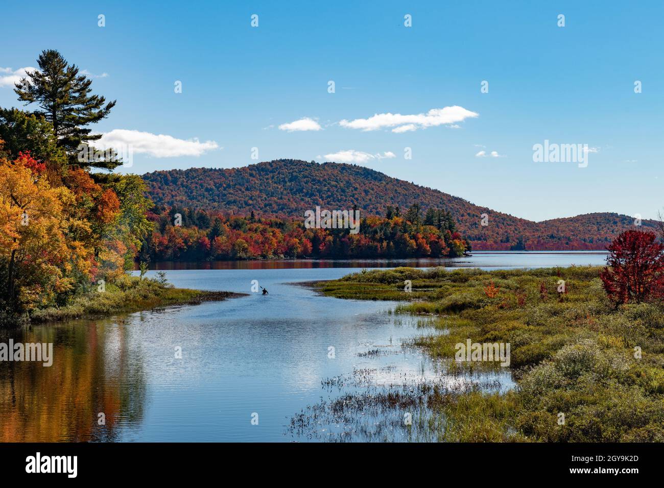 A view of a man paddling a canoe on Lewey Lake in the Adirondack Mountains, NY USA in autumn with fall colors on display Stock Photo