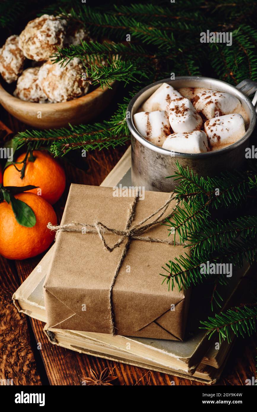Gift box wrapped with craft paper on stack of old books. Hot chocolate, spices and fruits Stock Photo