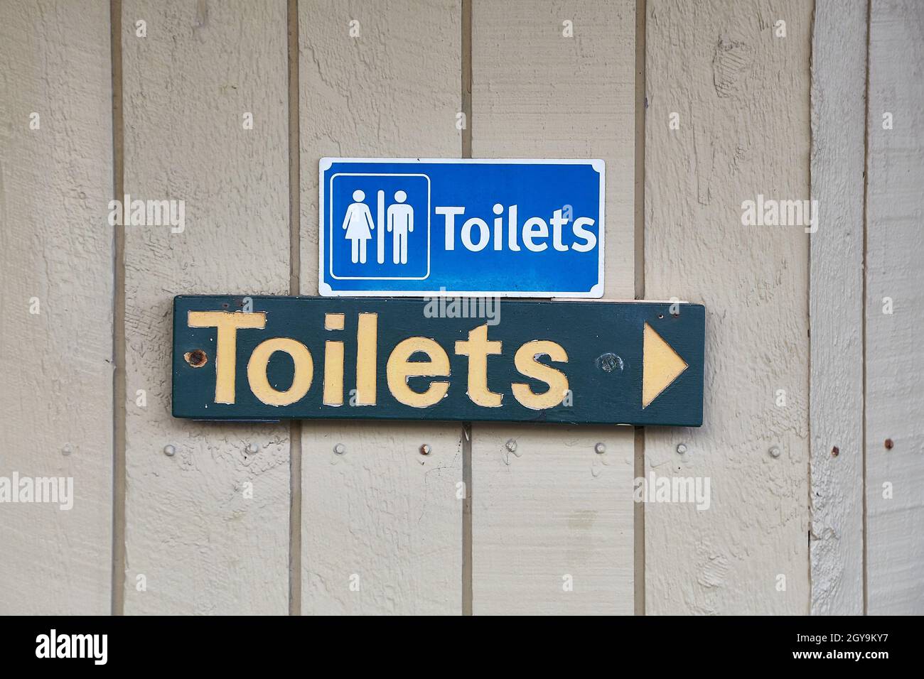 Public toilets signs on a wooden building, arrow shoing direction Stock Photo