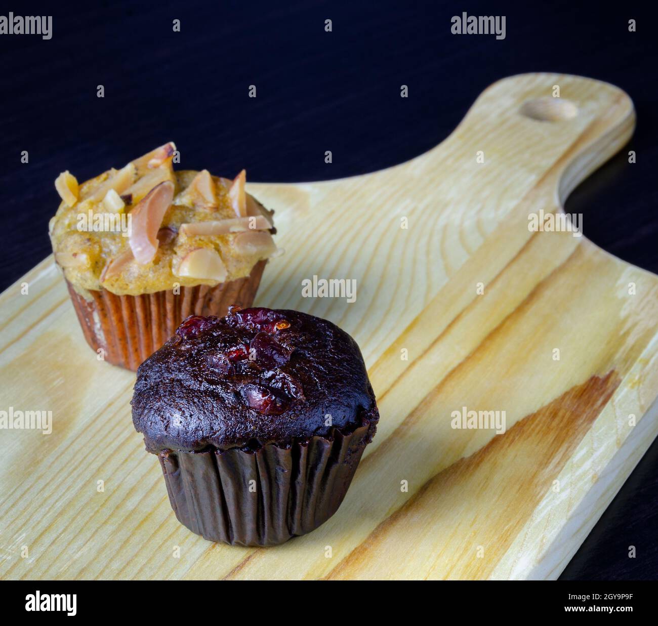 Chocolate cherry muffin and banana cupcake with almond toping on wooden board Stock Photo