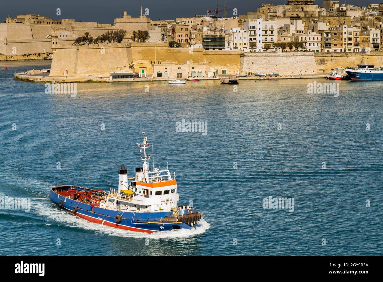 Working tug with waves and wake preparing to assist cruise liners in the Mediterranean sea in  Valetta Harbour Malta Stock Photo