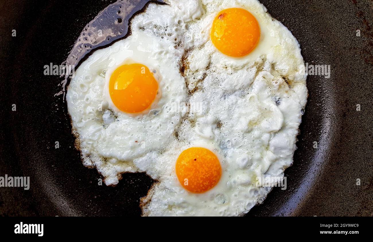 Three free range fried eggs in a hot non stick frying pan. Stock Photo