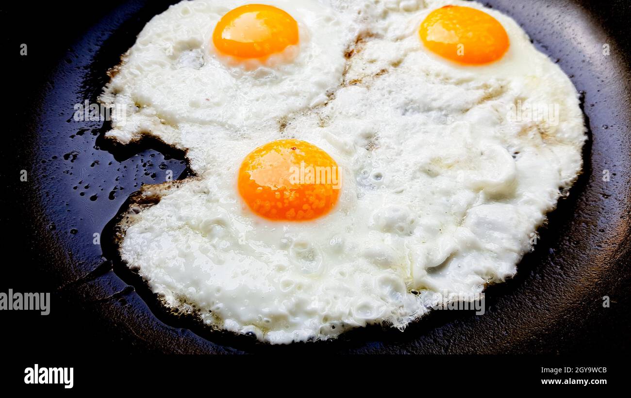 Three free range fried eggs in a hot non stick frying pan. Stock Photo