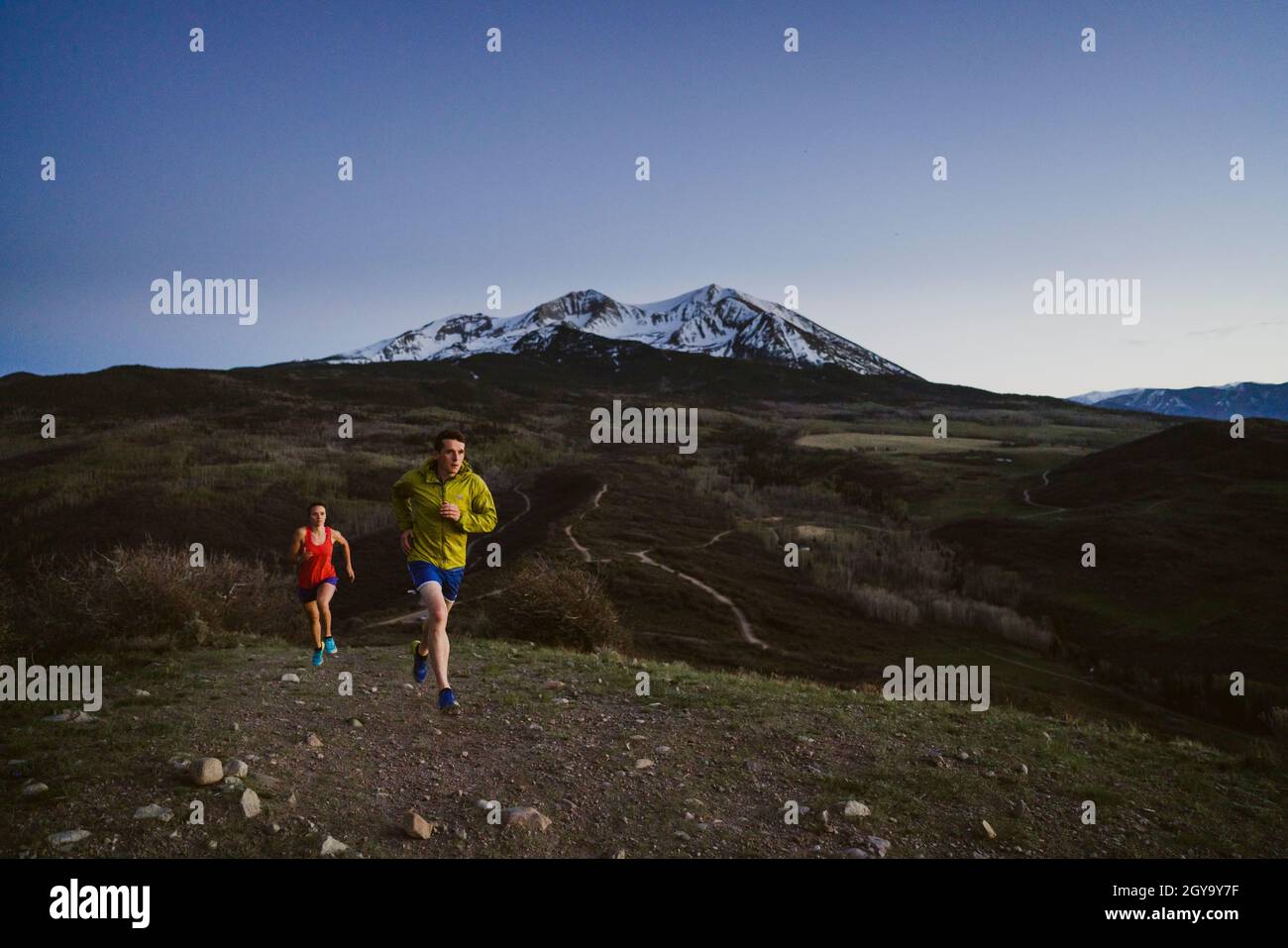 A man and woman trail run at dawn with mountains in the distance Stock Photo