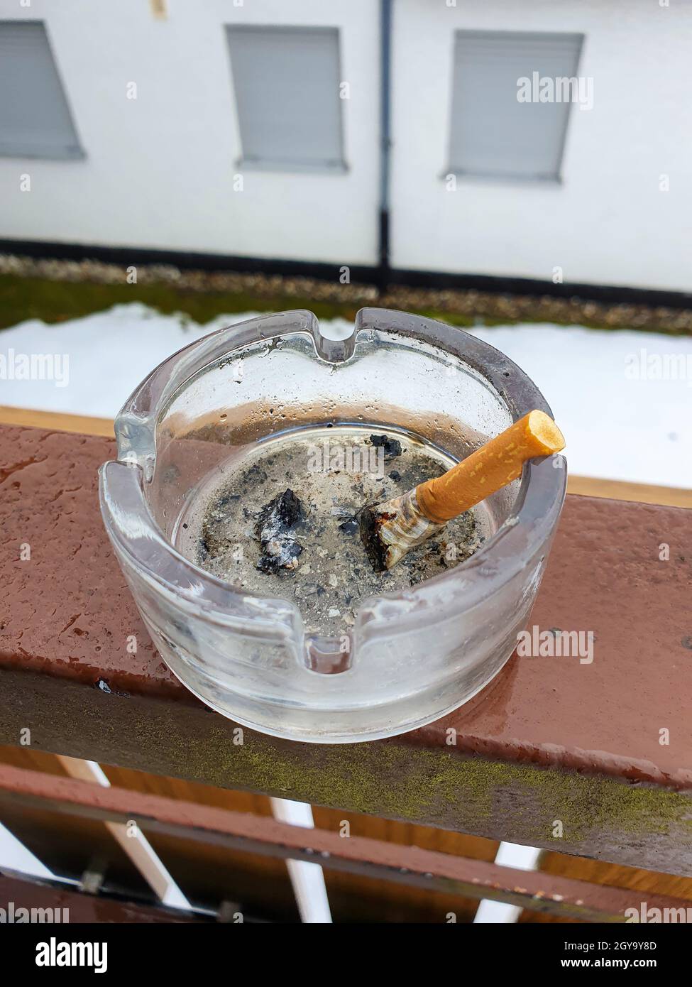 A stubbed out cigarette in an ashtray outside on the balcony. Stop