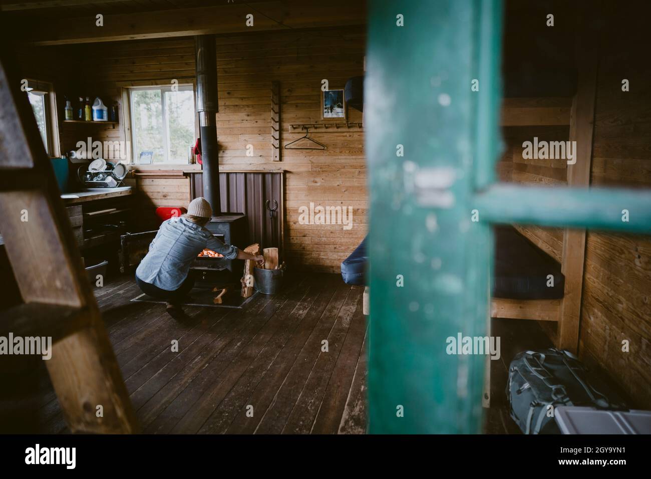 View through doorway of a woman stoking fire inside rustic cabin Stock Photo
