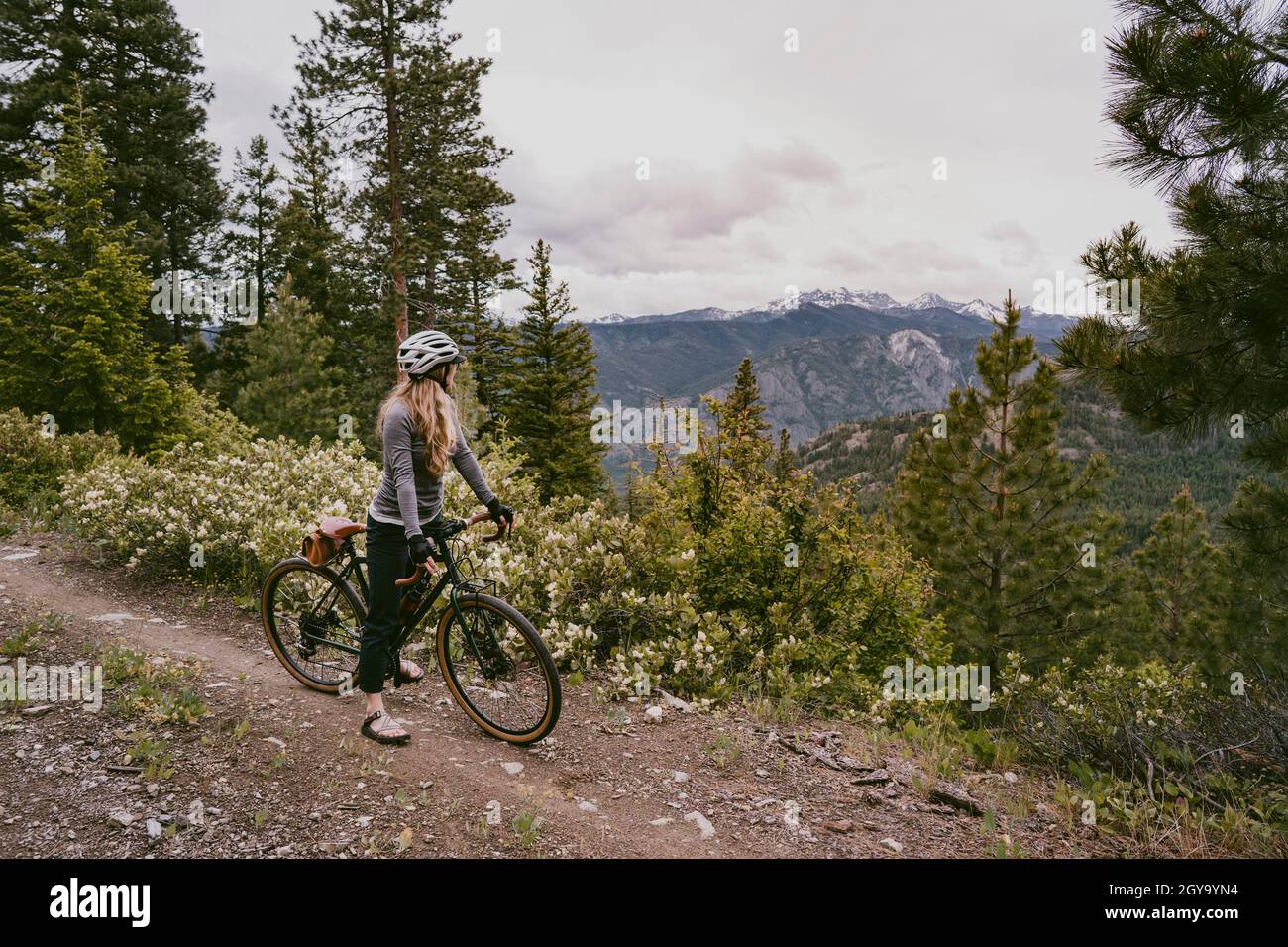 Woman bikes on rocky mountain trail and stops to enjoy view Stock Photo